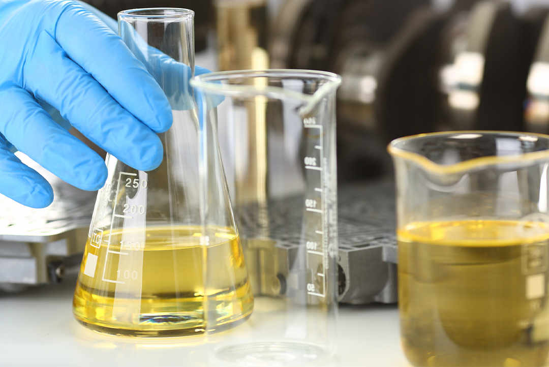 mão com luva manuseando frascos com óleo para análise.